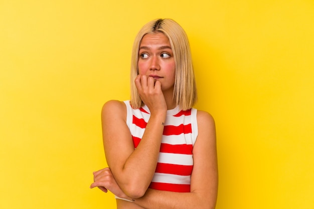 Jonge Venezolaanse vrouw geïsoleerd op gele muur vingernagels bijten, nerveus en erg angstig.