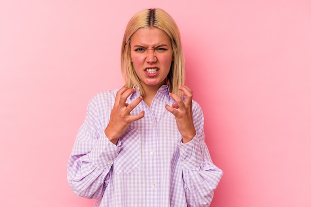 Jonge Venezolaanse vrouw geïsoleerd op roze achtergrond boos schreeuwen met gespannen handen.