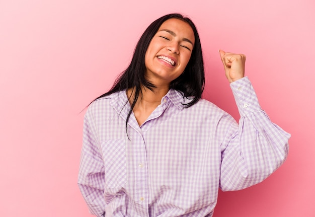 Jonge Venezolaanse vrouw geïsoleerd op roze achtergrond die een overwinning, passie en enthousiasme, gelukkige uitdrukking viert.