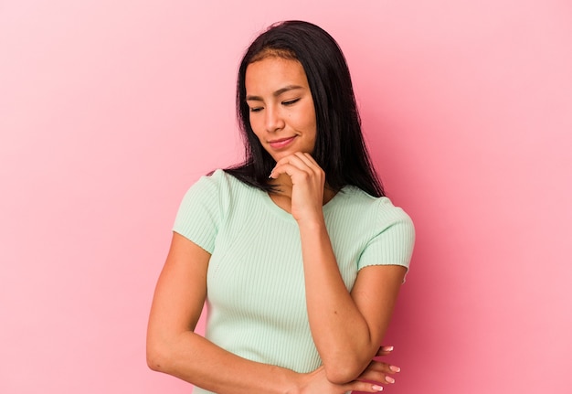 Jonge Venezolaanse vrouw geïsoleerd op roze achtergrond zijwaarts kijkend met twijfelachtige en sceptische uitdrukking.