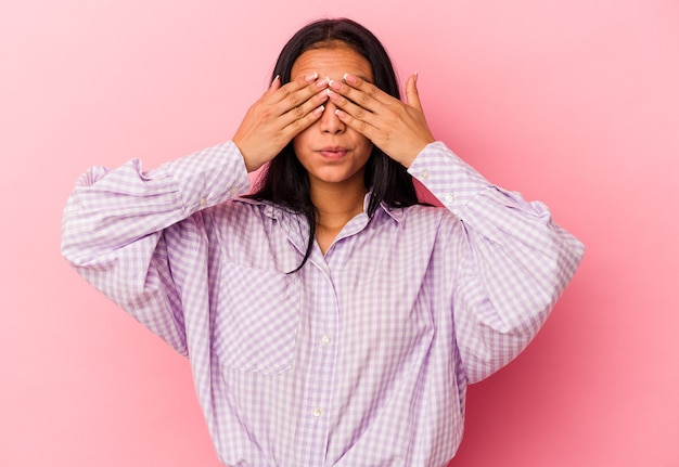 Jonge Venezolaanse vrouw geïsoleerd op roze muur bang voor ogen met handen.