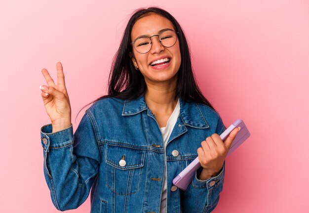 Jonge Venezolaanse vrouw met een tablet geïsoleerd op roze achtergrond blij en zorgeloos met een vredessymbool met vingers.