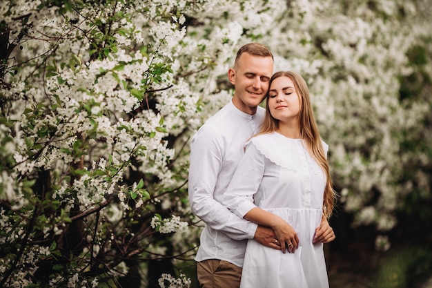 Jonge verliefde paar in een wandeling in een lente bloeiende appelboomgaard. Gelukkig getrouwd stel geniet van elkaar tijdens het wandelen in de tuin. Man die de hand van de vrouw vasthoudt