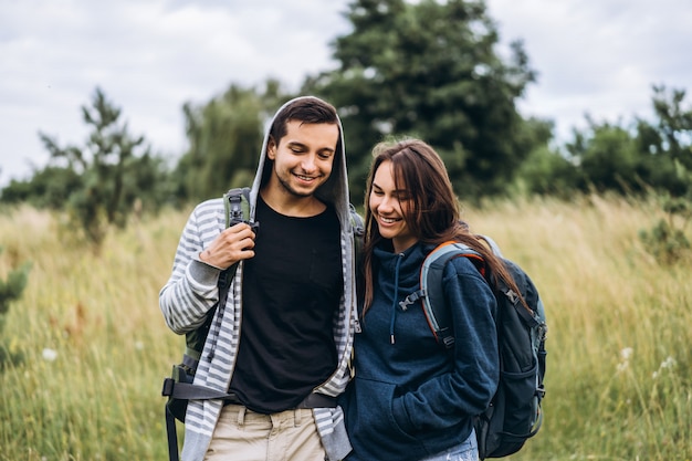 Jonge verliefde paar met rugzakken lopen en zachtjes knuffelen op het veld en de bomen. Liefdesverhaal