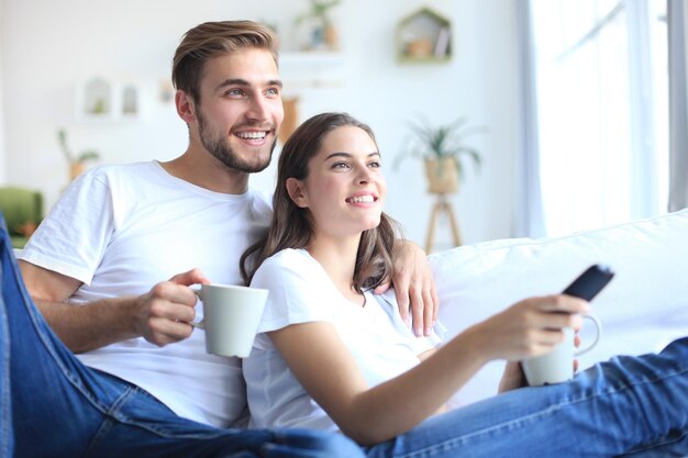 Jonge verliefde paar op de bank thuis tv kijken en lachen.