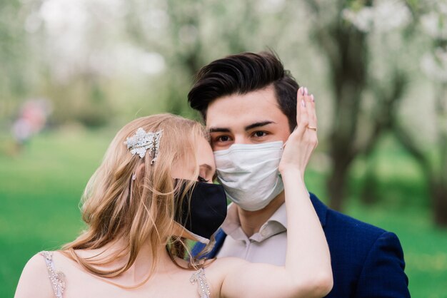 Jonge verliefde paar wandelen in medische maskers in het park tijdens quarantaine op hun trouwdag.