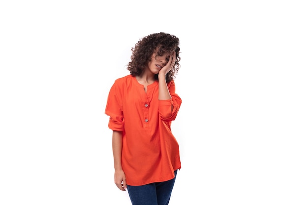 Jonge vermoeide blanke dame met zwart krullend haar gekleed in een oranje shirt dacht