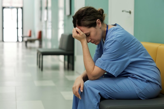 Jonge vermoeide of gestresste vrouwelijke arts die in de ziekenhuisgang zit