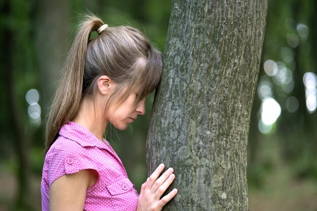 Jonge vermoeide vrouw rust leunend naar boomstam in zomer bos.