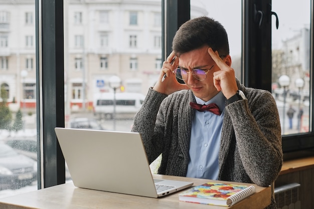 Jonge vermoeide zieke overwerkte man in formele slijtage zit achter de computer en aanraken van zijn voorhoofd