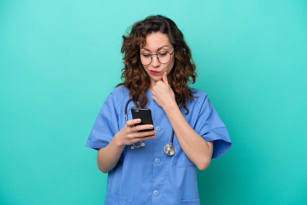 Jonge verpleegster blanke vrouw geïsoleerd op blauwe achtergrond denken en een bericht verzenden