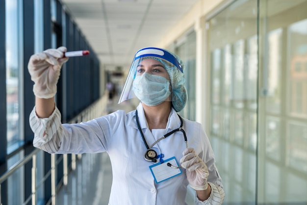 Jonge verpleegster in beschermend pak en gelaatsscherm met een positief bloedtestresultaat voor covid-19 in laboratorium. pandemie