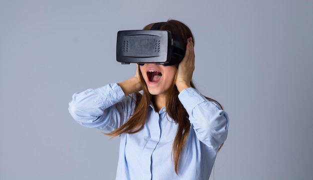 Jonge verraste vrouw in blauw shirt met Vr-bril op grijze achtergrond in studio