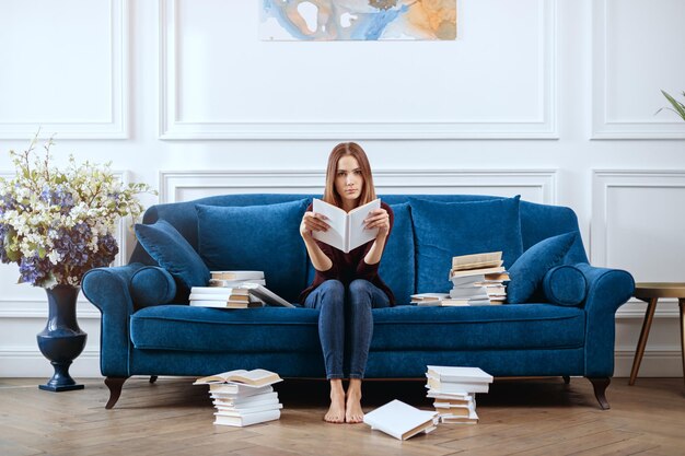 Jonge verveelde vrouw met een boek op een ruime bank in de woonkamer