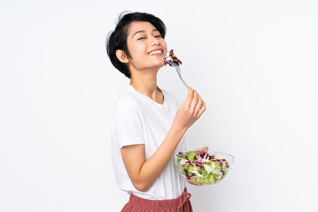 Jonge vietnamese vrouw die met kort haar een salade over muur houdt