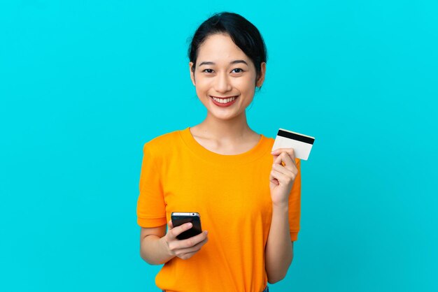Jonge vietnamese vrouw geïsoleerd op blauwe achtergrond kopen met de mobiel met een creditcard