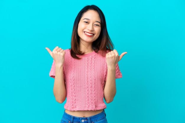 Jonge Vietnamese vrouw geïsoleerd op blauwe achtergrond met duim omhoog gebaar en lachend