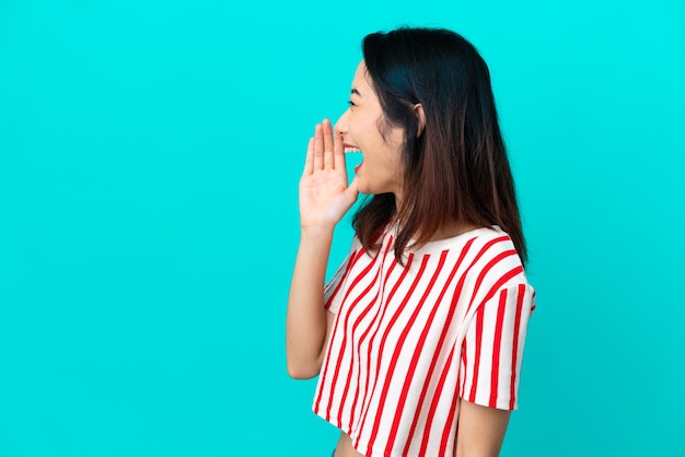 Jonge Vietnamese vrouw geïsoleerd op blauwe achtergrond schreeuwend met mond wijd open naar de zijkant