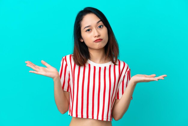 Jonge Vietnamese vrouw geïsoleerd op blauwe achtergrond twijfels gebaar maken