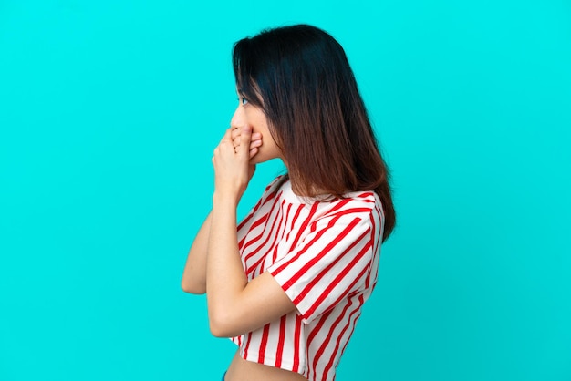 Jonge Vietnamese vrouw geïsoleerd op een blauwe achtergrond die de mond bedekt en naar de zijkant kijkt