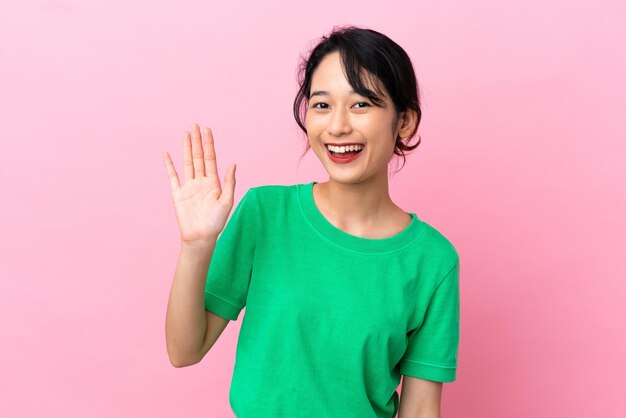 Jonge Vietnamese vrouw geïsoleerd op roze achtergrond die met de hand salueert met een gelukkige uitdrukking