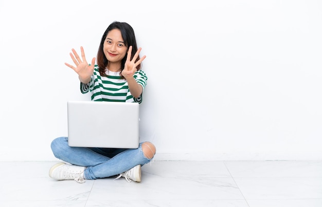 Jonge Vietnamese vrouw met een laptop zittend op de vloer geïsoleerd op een witte muur die acht met vingers telt