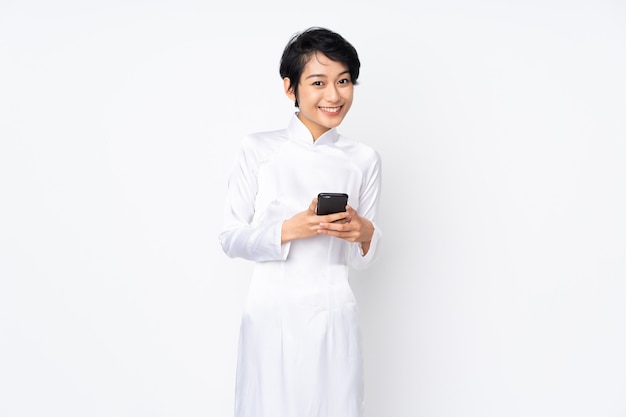 Jonge Vietnamese vrouw met kort haar dat een traditionele kleding over geïsoleerd wit draagt dat een bericht met mobiel verzendt