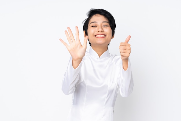 Jonge Vietnamese vrouw met kort haar die een traditionele kleding over geïsoleerd wit dragen die zes met vingers tellen