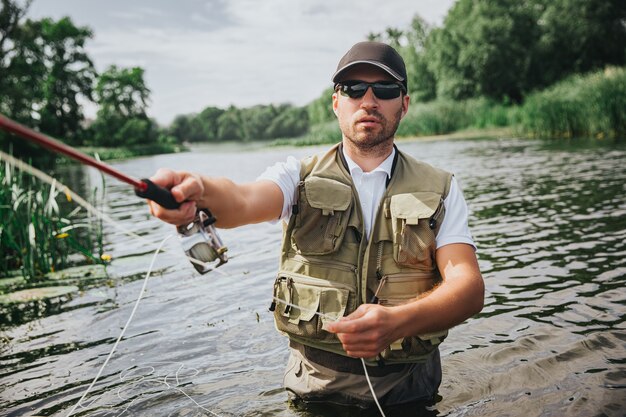 Jonge visser die op meer of rivier vist. Foto van de mens die actief vissen doet met een staaf in de hand. Sta alleen midden in rivier of meer. Ernstige geconcentreerde man aan het vissen.