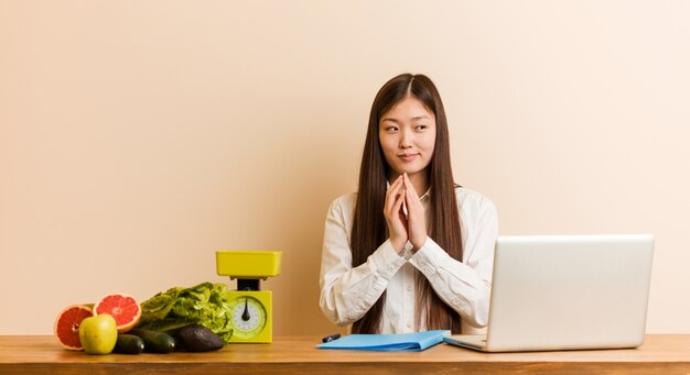 Jonge voedingsdeskundige Chinese vrouw die met haar laptop werkt die plan in mening opmaakt, die een idee opzet.