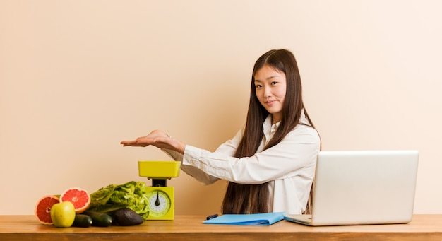 Jonge voedingsdeskundigenvrouw die met haar laptop werkt die een exemplaarruimte houdt aan een palm