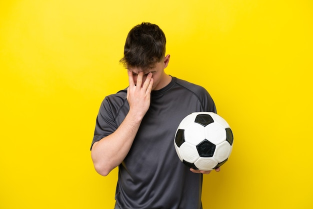 Jonge voetballer man geïsoleerd op gele achtergrond met vermoeide en zieke expressie