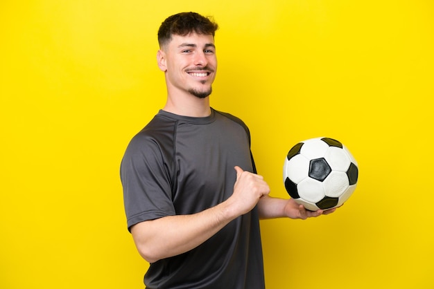 Jonge voetballer man geïsoleerd op gele achtergrond trots en zelfvoldaan