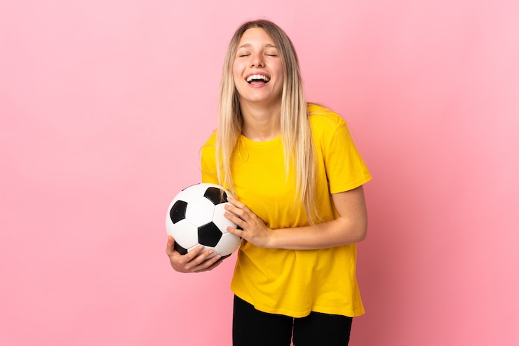 Foto jonge voetballer vrouw geïsoleerd op roze muur lachen