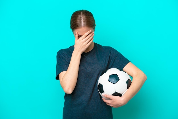 Jonge voetballervrouw die op blauwe achtergrond met vermoeide en zieke uitdrukking wordt geïsoleerd