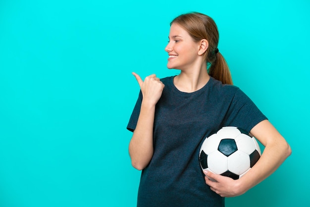 Jonge voetballervrouw die op blauwe achtergrond wordt geïsoleerd die naar de kant wijst om een product te presenteren