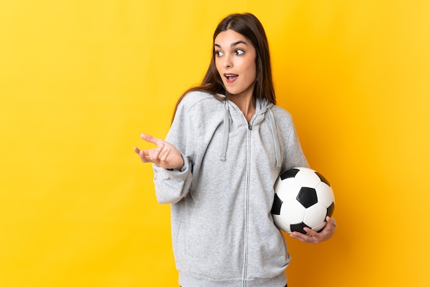 Jonge voetballervrouw die op geel met verrassingsuitdrukking wordt geïsoleerd terwijl zij kant kijkt