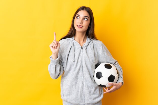 Jonge voetballervrouw die op gele achtergrond wordt geïsoleerd die een geweldig idee benadrukt