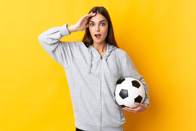 Jonge voetballervrouw die op gele muur met verrassingsuitdrukking wordt geïsoleerd