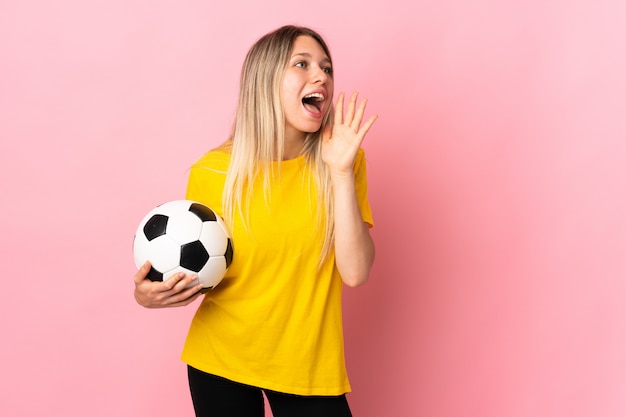 Jonge voetbalstersvrouw die bij de roze muur wordt geïsoleerd die met wijd open mond schreeuwen