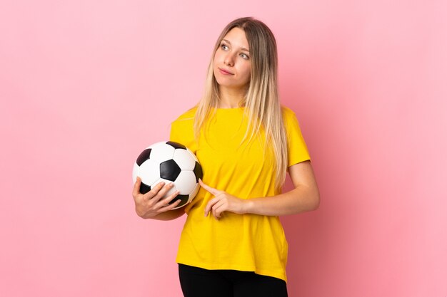 Jonge voetbalstersvrouw die op roze muur wordt geïsoleerd die kant kijkt