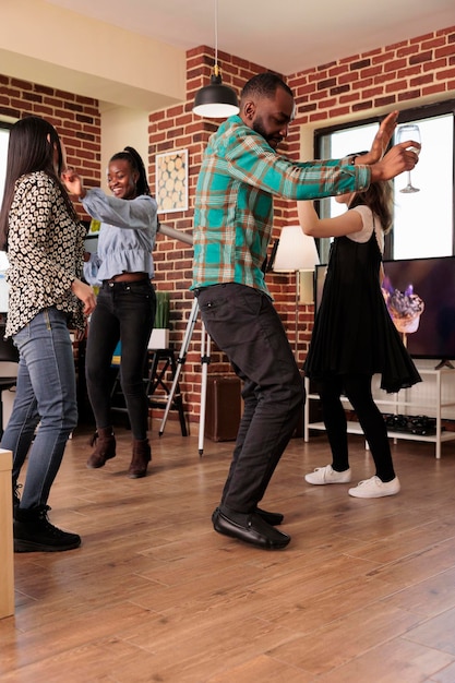 Jonge volwassen Afro-Amerikaanse mannelijke verticale schot dansen op verschillende etnische groepen mensen feest, bijeenkomst, reünie. Verschillende nationaliteiten vriendengroep die wijn drinkt, genietend van vriendschap.