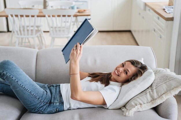 Jonge volwassen blanke vrouw leest boek thuis tot op de bank Mooie Spaanse vrouw geniet van geletterdheid