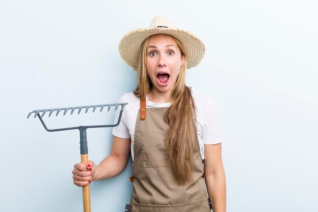 Jonge volwassen blonde vrouw boer met een hark