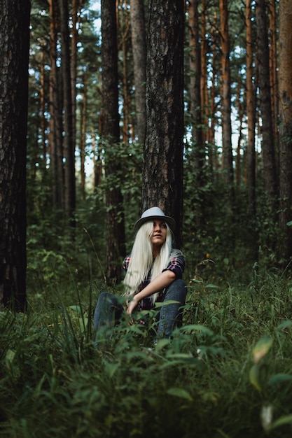 Jonge volwassen blonde vrouw in een hoed zitten in het bos