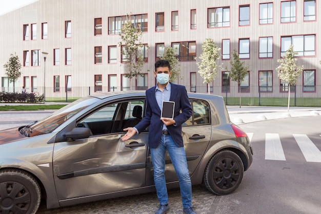 Jonge volwassen brunette verzekeringsagent met chirurgisch medisch maskerjasje en spijkerbroek geïnspecteerd gedeukte auto na verkeersongeval met deuken en krassen op de deur van het voertuig Buiten schot