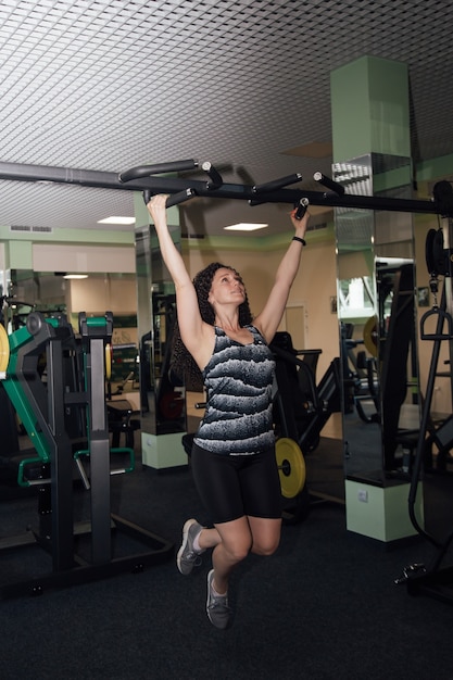 Jonge volwassen fitnessvrouw die zich voorbereidt om pull-ups te doen in de optrekstang.