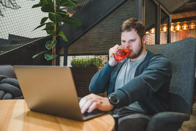 Jonge volwassen man aan het werk op laptop in café. fruitthee drinken. freelance levensstijl