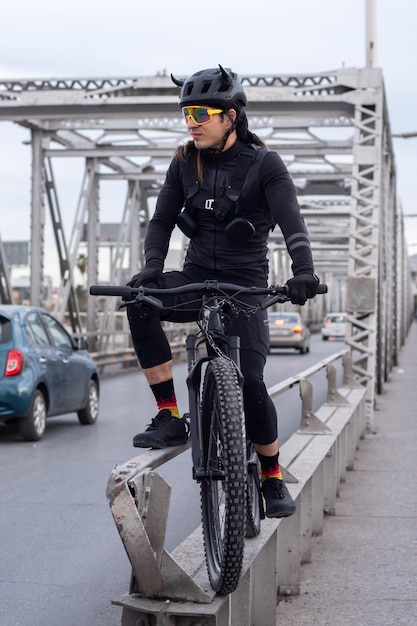 Jonge volwassen man met fietsuitrusting bij stedelijke stalen brug