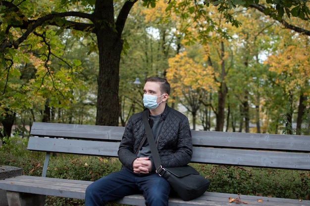 Jonge volwassen man zit op een bankje in donkere kleren, groen park herfst